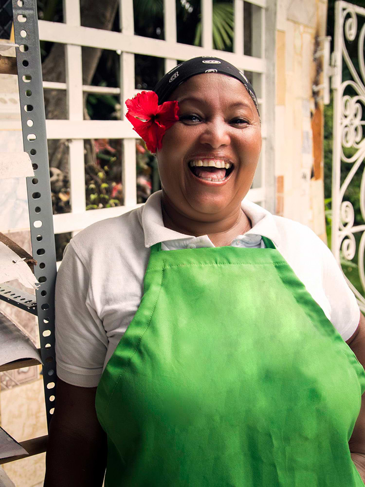 Woman smiling with a green apron on and flower behind ear