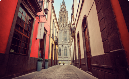A narrow walkway in an old city reveals a beautiful cathedral at the end.