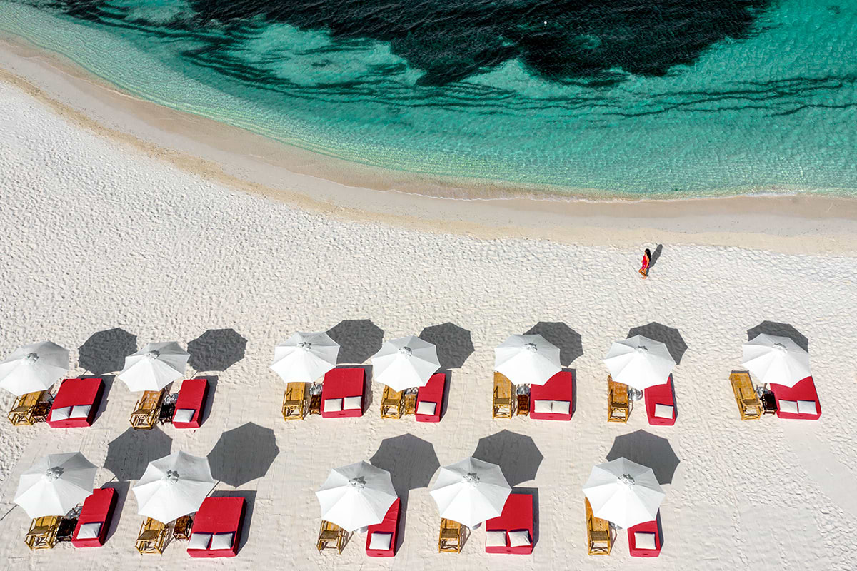 Aerial view of a woman walking at the beach and beach umbrellas and chairs lined