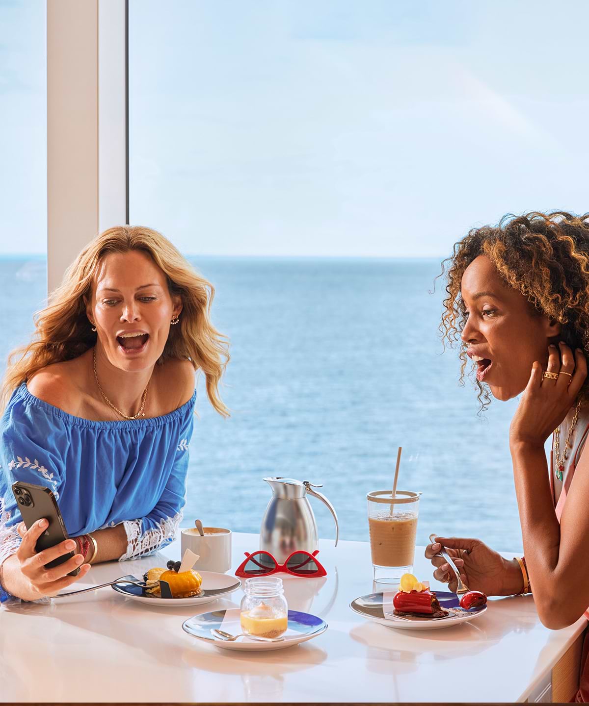 women at dinner table reacting to phone with ocean view in the background
